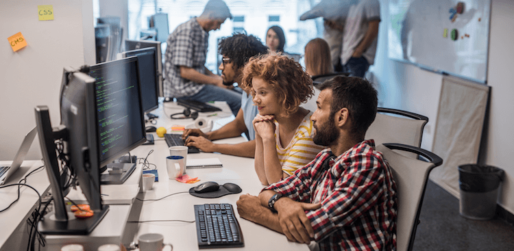 people sitting in an office working on computers with code onscreen