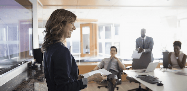 person standing in front of co-workers in a conference room smiling