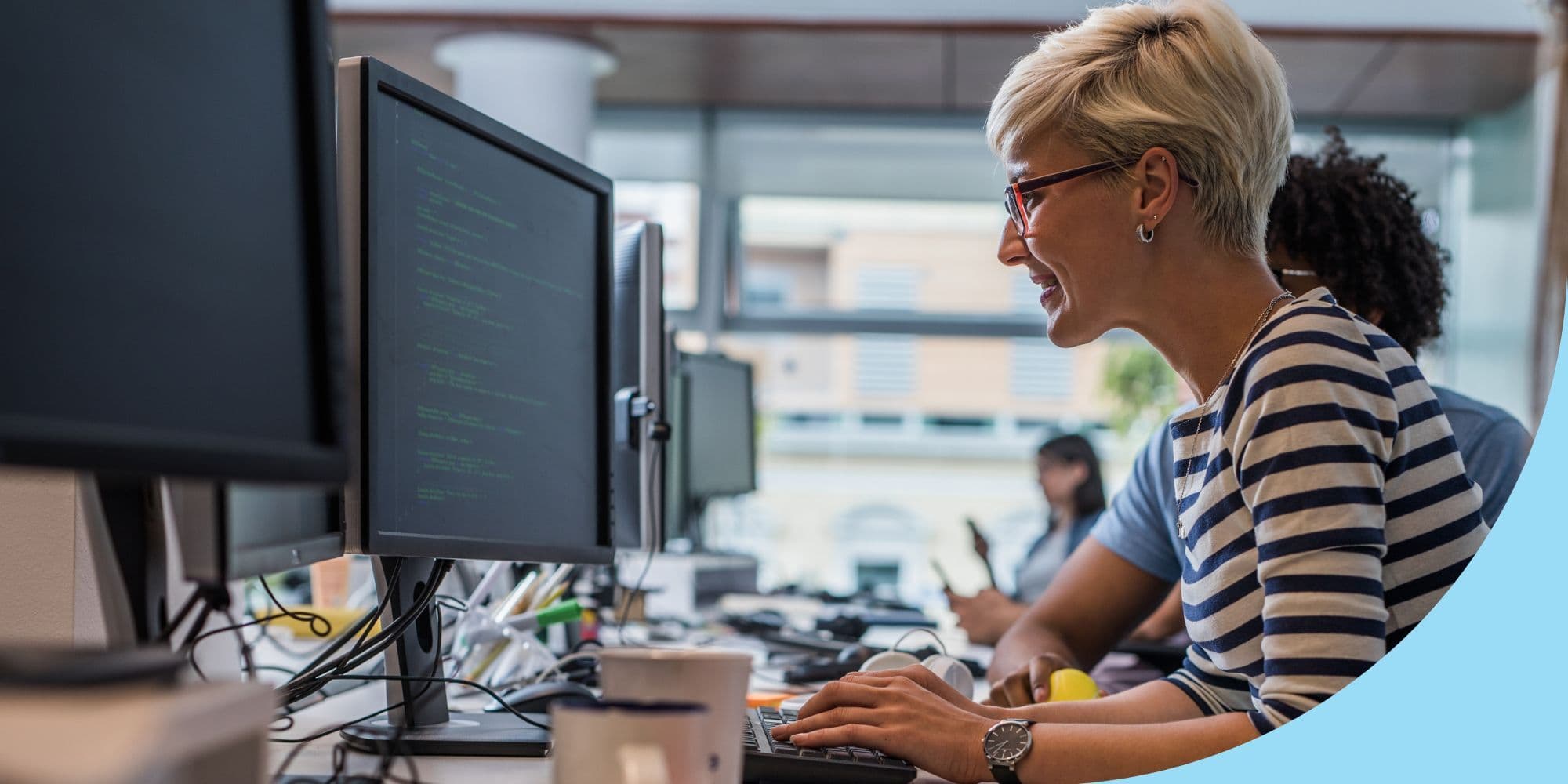 software developer working on a computer in an open office with windows visible in the background